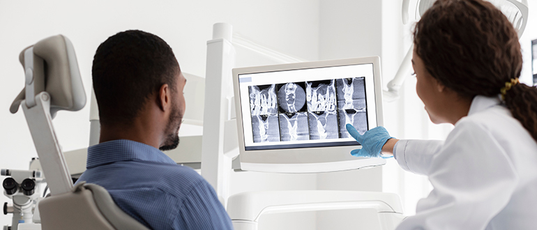 African,Female,Dentist,And,Male,Patient,Watching,Xray,On,Digital